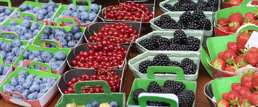 Baskets of Fresh Berries at Fruit Market with natural ripe colorful nutritious blackberries strawberries and blueberries