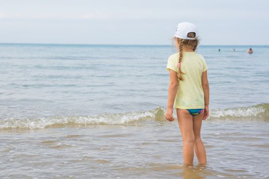 Girl dressed in a T-shirt standing on a beach and looks into the distance to the sea