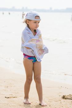 hree year old girl standing on the beach wrapped in a towel in cold windy weather