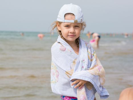 Three year old girl standing on the beach wrapped in a towel in cold windy weather