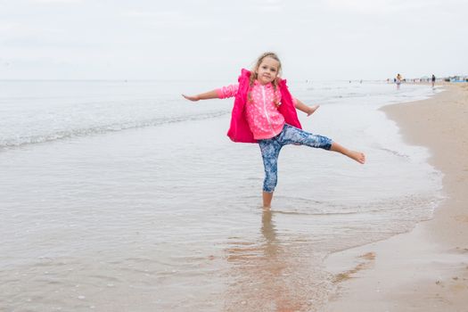 Three year old girl having fun stood on one leg on the beach in the cool overcast weather