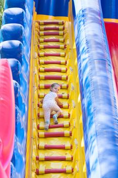 Three year old girl climbs the stairs to the high hill inflatable trampoline
