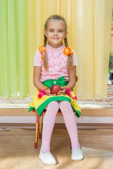 Six year old girl sitting on a chair and holding an apple in his hand on a matinee in kindergarten