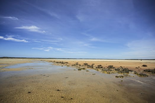 Perfect beach scene of low  tide, interesting rock formations and pristine white sand and bright blue sky