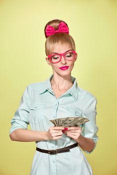 Beauty fashion. Money, banking finance concept. Business woman with dollar bill, cash smiling.Confidence, Pinup hairstyle, pink bow, glasses.Unusual playful, emotion. Shopping happy girl thinking idea