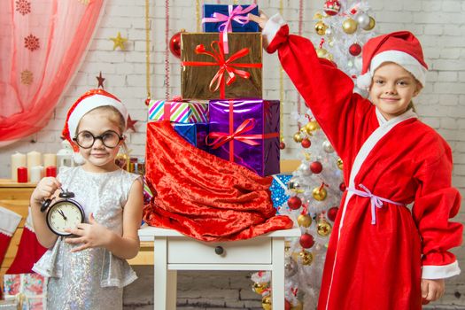Two girls sisters four and six years in the New Year costumes are at the bag with Christmas gifts