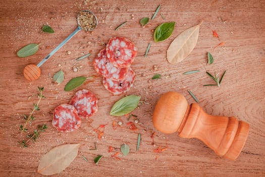 Sliced sausage salami with herbs and spices ,thyme, rosemary, saffron,basil, pepper, and oregano on the teak wood table .