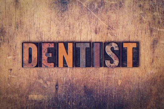 The word "Dentist" written in dirty vintage letterpress type on a aged wooden background.
