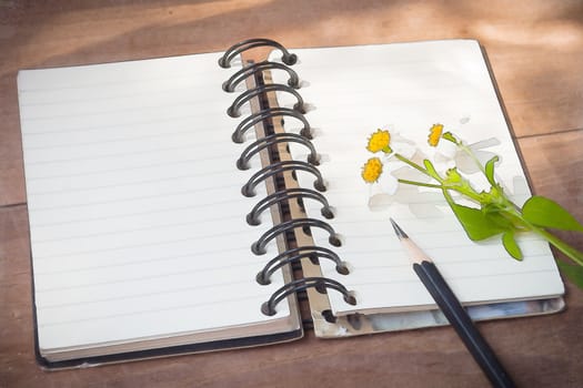 Notebook with black pencil, white flowers on wooden table