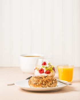 Simple healthy breakfast of a muesli bagel with coffee and a fruit parfait.