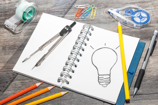 Office supplies and an open book with a drawing of a light bulb