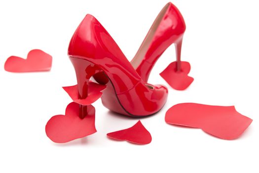 Red shoes with a high heel and stomped and strung on a hairpin of the heart on a white background