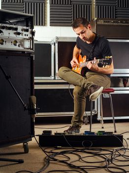 Photo of a man in his late 20's sitting in a recording studio practicing his guitar playing.