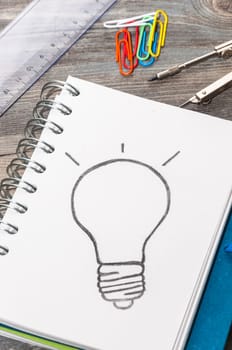 Office supplies and an open book with a drawing of a light bulb