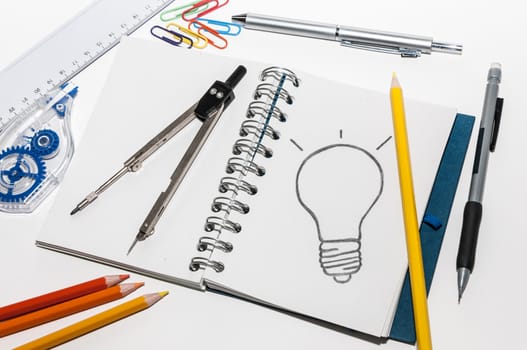 Office supplies and an open book with a drawing of a light bulb