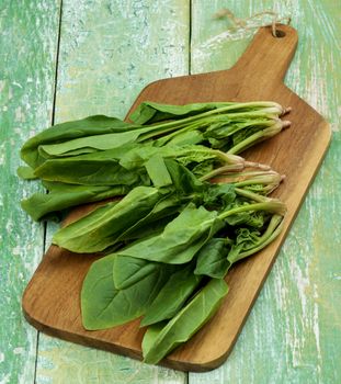 Heap of Raw Spinach Leafs Ion Wooden Cutting Board closeup on Cracked Green Wooden background