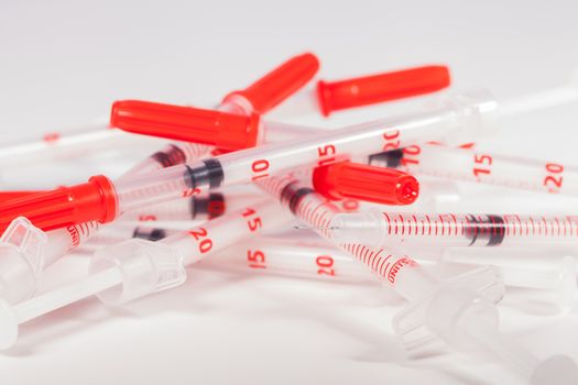 Still Life Close Up of Pile of Empty Syringe Needles with Red Safety Caps in Studio with White Background