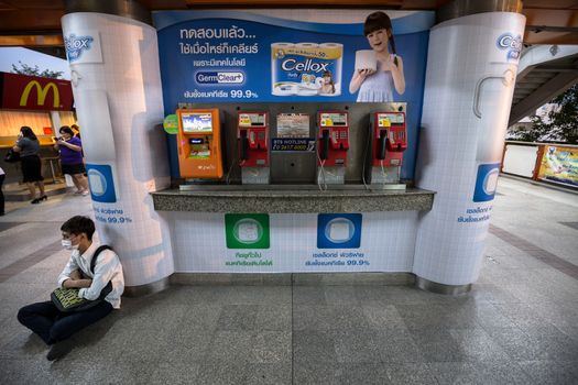 Bangkok, Thailand - January 18, 2016 : public payphone and top up machine on the corner with advertisement poster in Thai language in the background at BTS Mo Chit station in the evening with unidentified man sitting in the corner.