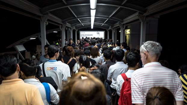 Bangkok, Thailand - January 18, 2016 : Crowd of people walking out from the BTS Mo Chit station to the road in the rush hour at night. They have to walk cross a footbridge along with lights and advertising board. Daily passengers of BTS skytrain is around 700,000.