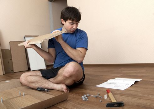 Young man puzzled aboutassembling flatpack closet