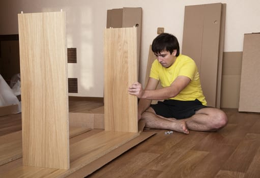 Young man sitting on floor assembling flatpack closet