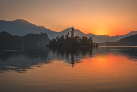 Little Island with Catholic Church in Bled Lake, Slovenia at Beautiful Colorful Sunrise with Castle and Mountains in Background