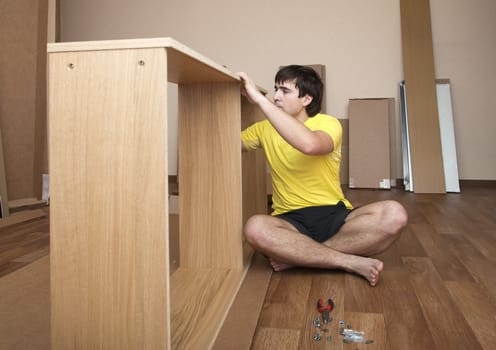 Young man sitting on floor assembling flatpack closet