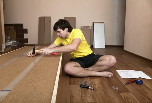 Young man sitting on floor assembling flatpack closet