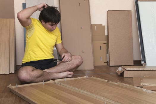 Young man in trouble assembling furniture at home
