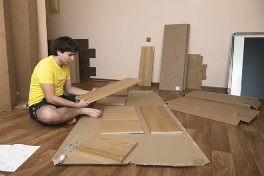 Young man sitting on floor assembling flatpack closet