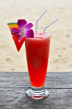 High glass full of cold fresh squeezed watermelon juice or cocktail with two straws on wooden table outside in beach cafe