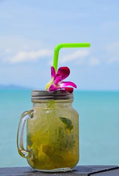 Big jars mug style full glass of fresh frozen mojito with metal cap lid, straw and purple orchid flower in cafe on the beach