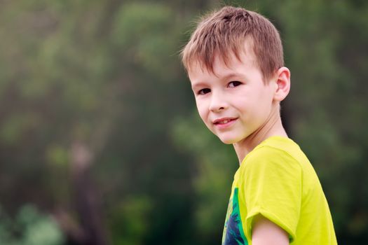 Portrait of a young boy with woods in the background. He's wearing a bright green t-shirt and has scruffy hair.