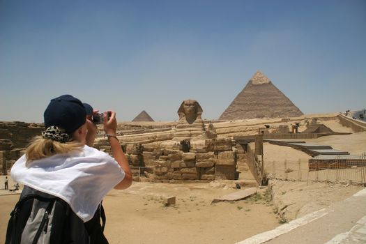 Blonde female turist takin picture of the Sphinx and the pyramids of Khafre (Chephren) and Menkaur (Mycerinus) in Giza - Cairo, Egypt