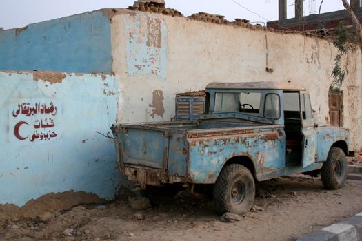 Old SUV in the desert oazis town by the blue building with verses from Koran on the wall