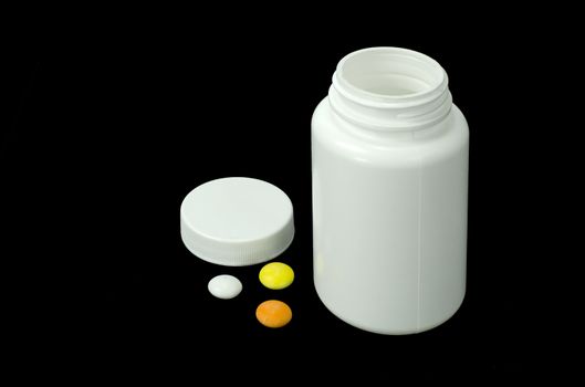 three pills of a different colors with white jar on a black background
