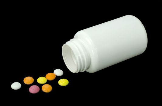 some pills of a different colors with white jar on a black background