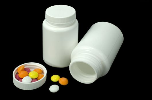 some pills of a different colors with two white jar on a black background