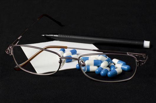Pen, tablet, prescription and glasses on a dark background