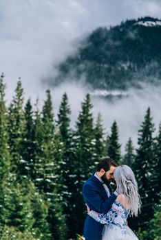 groom in a blue suit and bride in white, embroidered with blue pattern, dress on a background of green pine forests in the mountains of the Carpathians