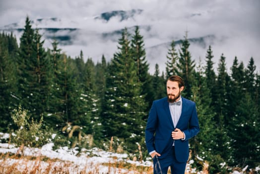 groom in a blue suit and bride in white, embroidered with blue pattern, dress on a background of green pine forests in the mountains of the Carpathians