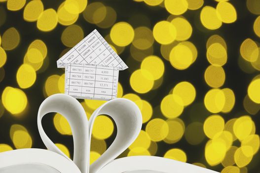 House on book as heart shape with defocused of glitter or golden bokeh circle at night as background.