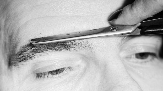 Portrait of man removing eyebrow hairs with scissors