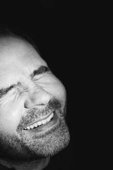 Close-up of mature smiling man to the brightness, closed eyes, low key, black and white