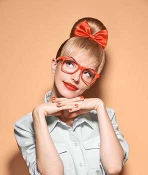 Beauty fashion woman in stylish glasses thinking, idea. Attractive pretty blonde hipster girl smiling. Confidence, success, Pinup hairstyle,red bow makeup. Unusual playful, expression.Vintage, vanilla