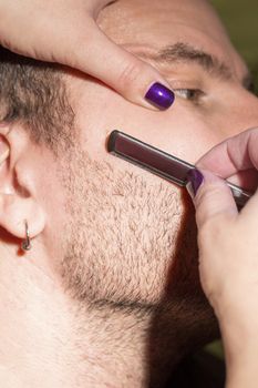 Hairdresser, cutting beard of his customer with scissors and shave in the salon