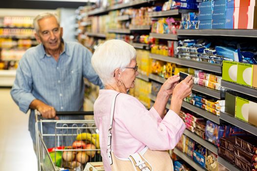 Senior woman taking a picture of product on shelf in supermarket 