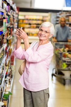 Senior woman taking a picture of product on shelf in supermarket 