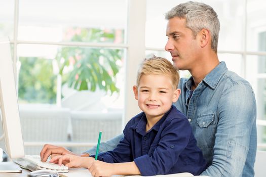 Father and son at the desk using computer and drawing