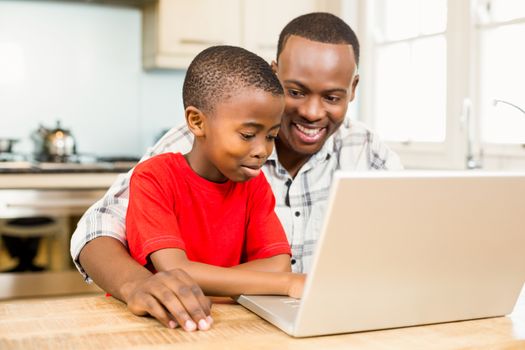 Father and son using laptop together in the kitchen